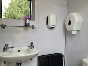 Internal view of Bear Loo with hand dryer, toilet roll holder and white ceramic fittings